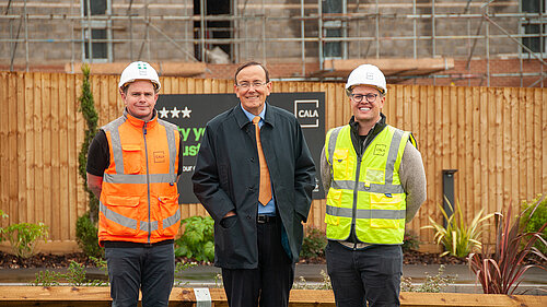 Three men - two in hi vis - one (Martin Tod) in a suit and coat - standing in front of a construction site with a Cala sign