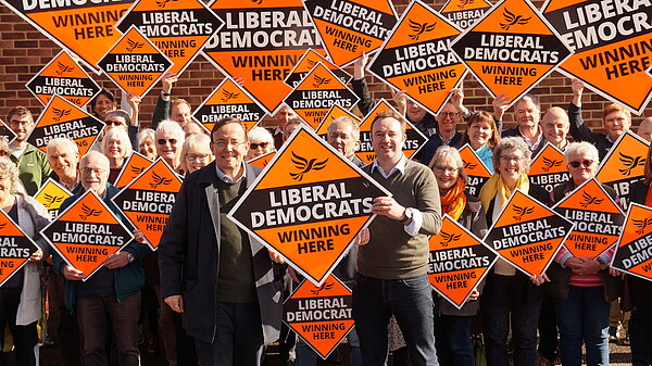 A group of people holding fluorescent orange "Liberal Democrats Winning Here" diamonds - with Martin Tod and Danny Chambers standing at the front
